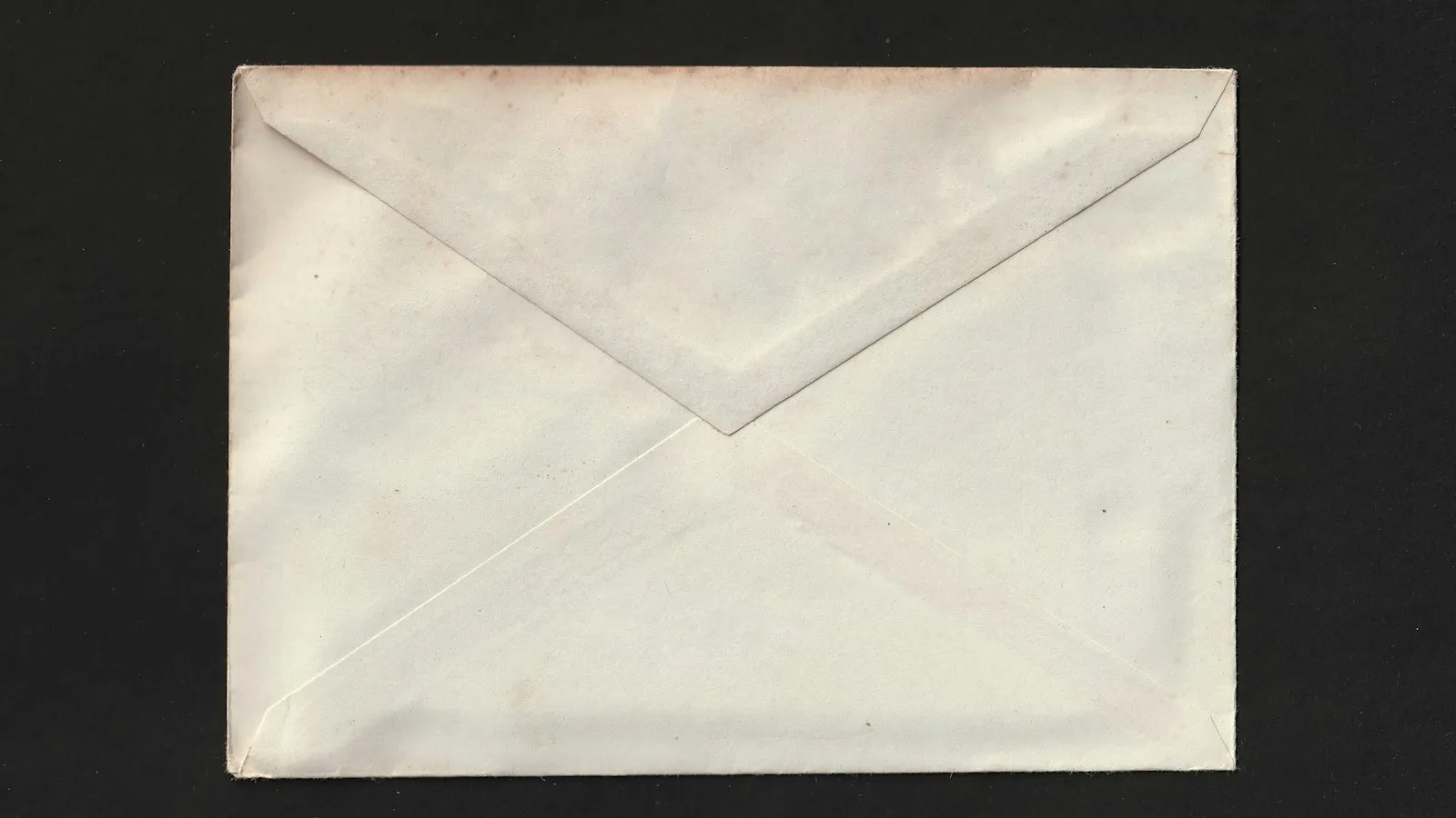 Enveloppe blanche en papier vieilli posée seule sur un fond noir, cadrage épuré et lumière douce aux tons gris